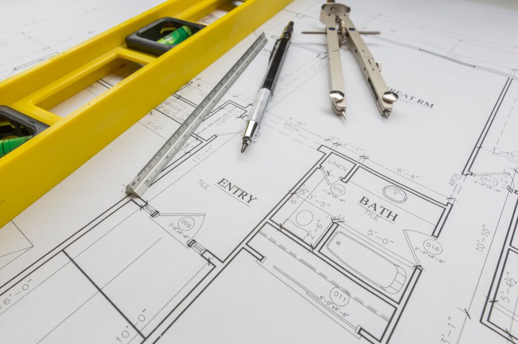 Construction Level, Engineer Pencil, Ruler and Compass Resting on Custom House Plans.